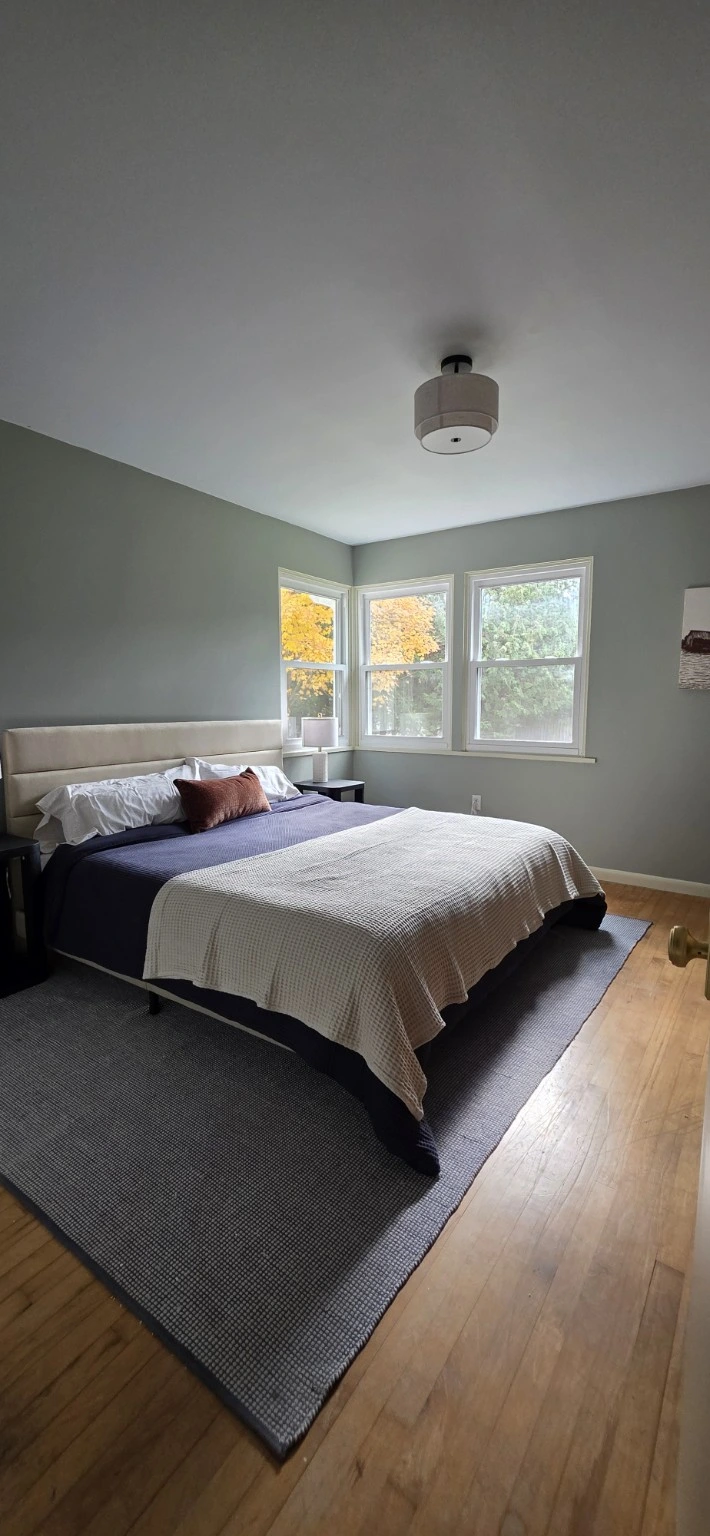 A furnished bedroom with layered bedding and leafy views