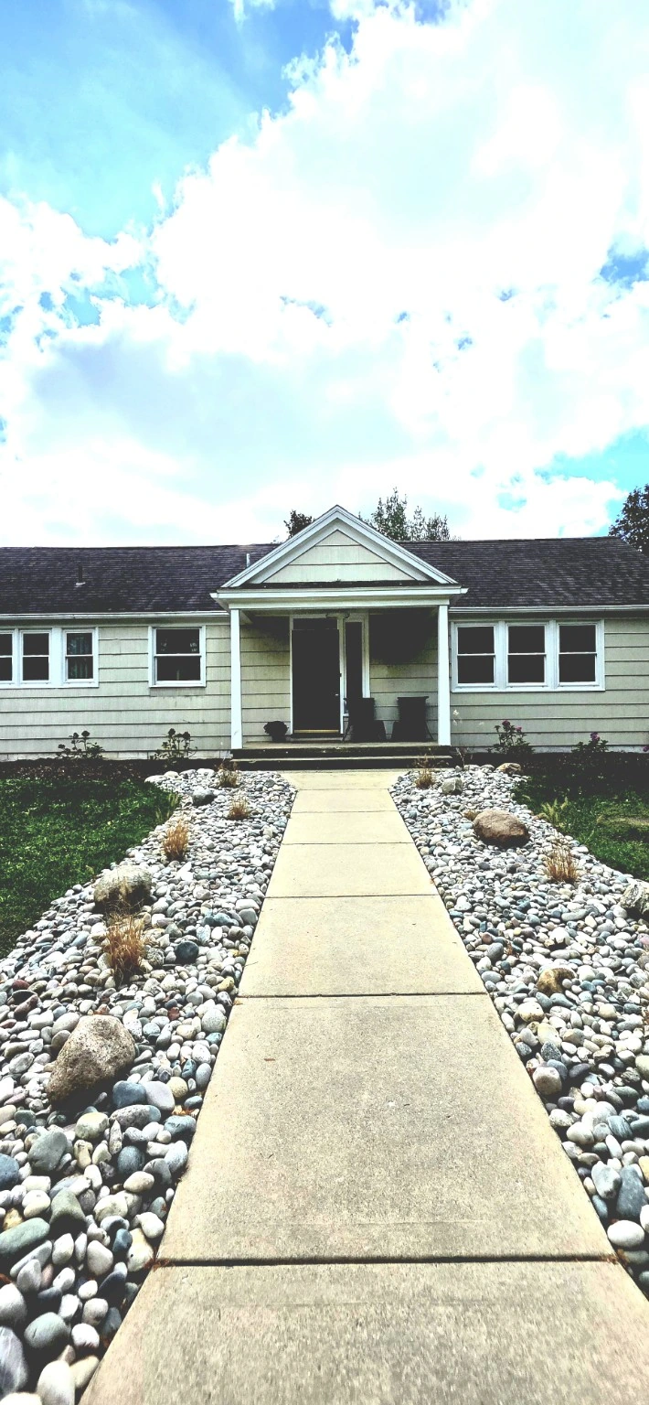 The front entrance of The Mill Street House, with a stone-lined walkway, porch chairs, and blue sky with clouds